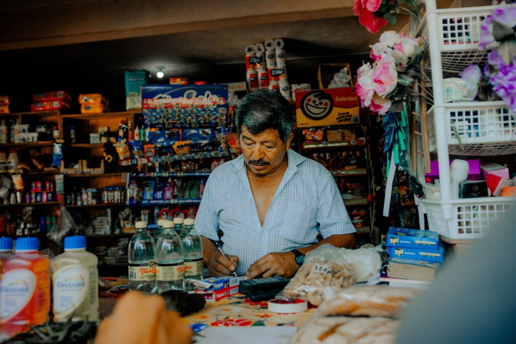 A man operating his shop filled with various merchandise, selling daily essentials.